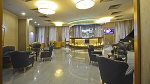 A lobby with a bar area, seating, and a piano. - Astoria Tbilisi (Tbilisi)