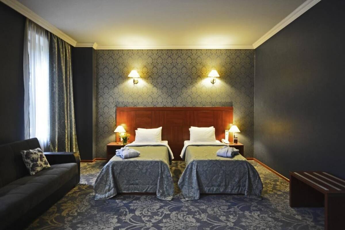 Ein Hotelzimmer mit zwei Betten, einem Sofa und einem großen Fenster mit Vorhängen.