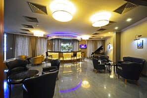 Vestíbulo de hotel con zona de bar, asientos, un piano y una televisión.