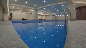 An indoor swimming pool with clear blue tiles, a tiled deck, and a modern ceiling with recessed lighting. - Astoria Tbilisi (Tbilisi)