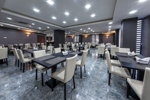 Un amplio salón de conferencias con varias mesas y sillas, suelo de mármol e iluminación empotrada en el techo.