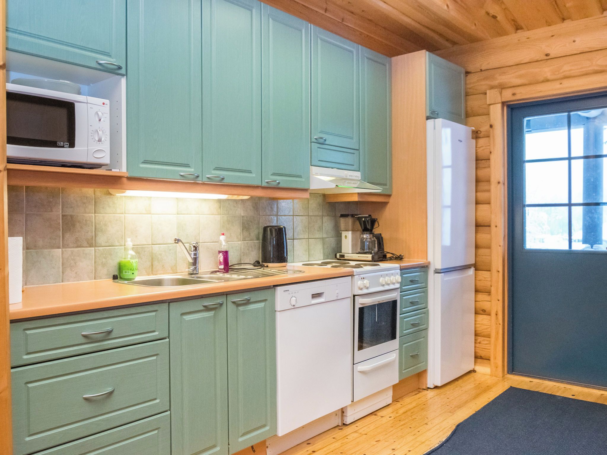 Une cuisine compacte avec des meubles de couleur turquoise, un four à micro-ondes, une machine à café, un lave-vaisselle et un réfrigérateur.