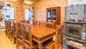 A wooden dining room with a large table and chairs, a cabinet with glass doors, and a stone fireplace. - Karhunpesä a by Interhome (Puolanka)