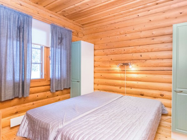 Een kamer in chaletstijl met een bed, houten wanden, een raam met gordijnen en een nachtkastje.