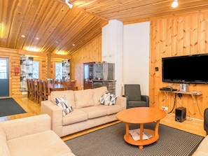 Een knus houten chalet interieur met een bank, een televisietoestel en een eethoek.