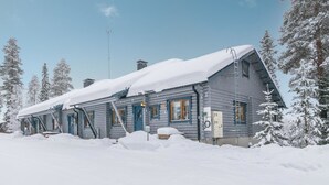 A log cabin with a snow-covered roof and a small porch, surrounded by snow-covered trees. - Karhunpesä a by Interhome (Puolanka)