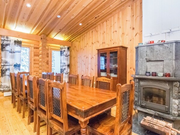 Comedor de madera con una mesa grande y sillas, chimenea y ventana con cortinas.