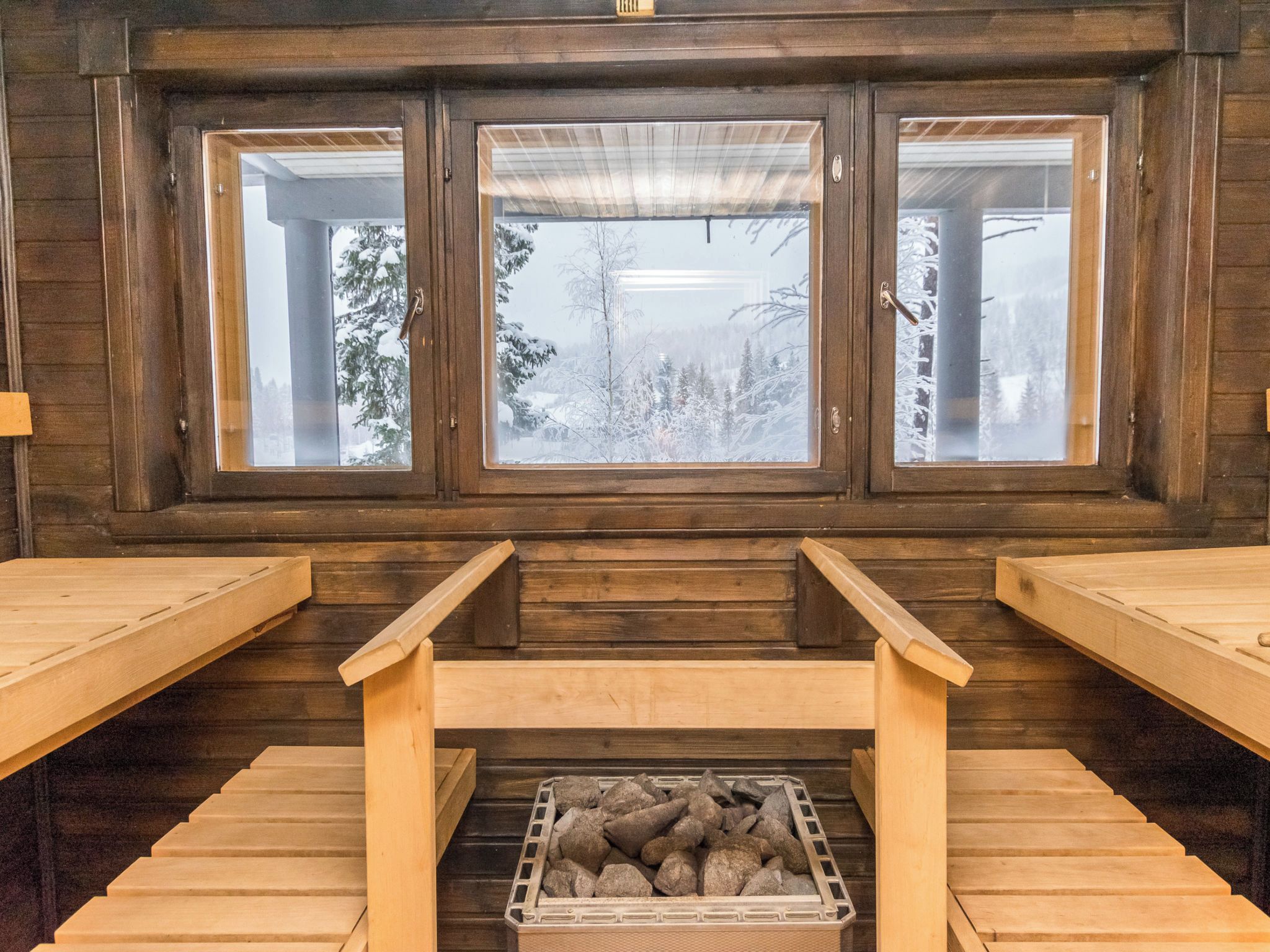 A sauna room with three wooden windows, a wooden bench, and a stone-filled container.
