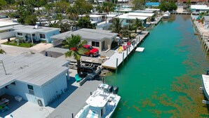 A marina with boats docked, a small building with a blue roof, and a dock with chairs and a red car. - Oceanside, Pet Friendly, Smart Home with-SUP, kayak with and 60 ft Dock (Marathon)