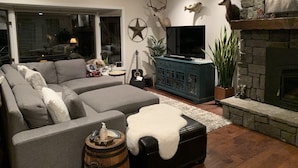 Ein modernes Wohnzimmer mit einer Eckcouch, einem Flachbildfernseher, dekorativen Geweihen und einem Kamin aus Stein.