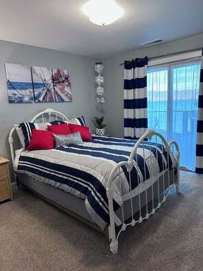 A bedroom with a bed, a nightstand, a potted plant, a wall-mounted light fixture, and a window with curtains.