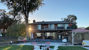Ein zweistöckiges Haus mit einer Terrasse, die Gartenmöbel und eine überdachte Sitzgruppe bietet.