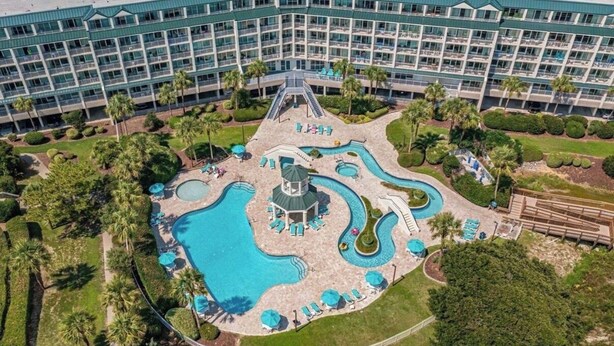 Um hotel com vários andares, uma piscina central com escorrega e palmeiras ao redor.