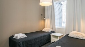 A bedroom with two beds, a small white nightstand, a lamp, and a window with curtains. - Skivillas paljakka 6. (2mh) by Interhome (Puolanka)