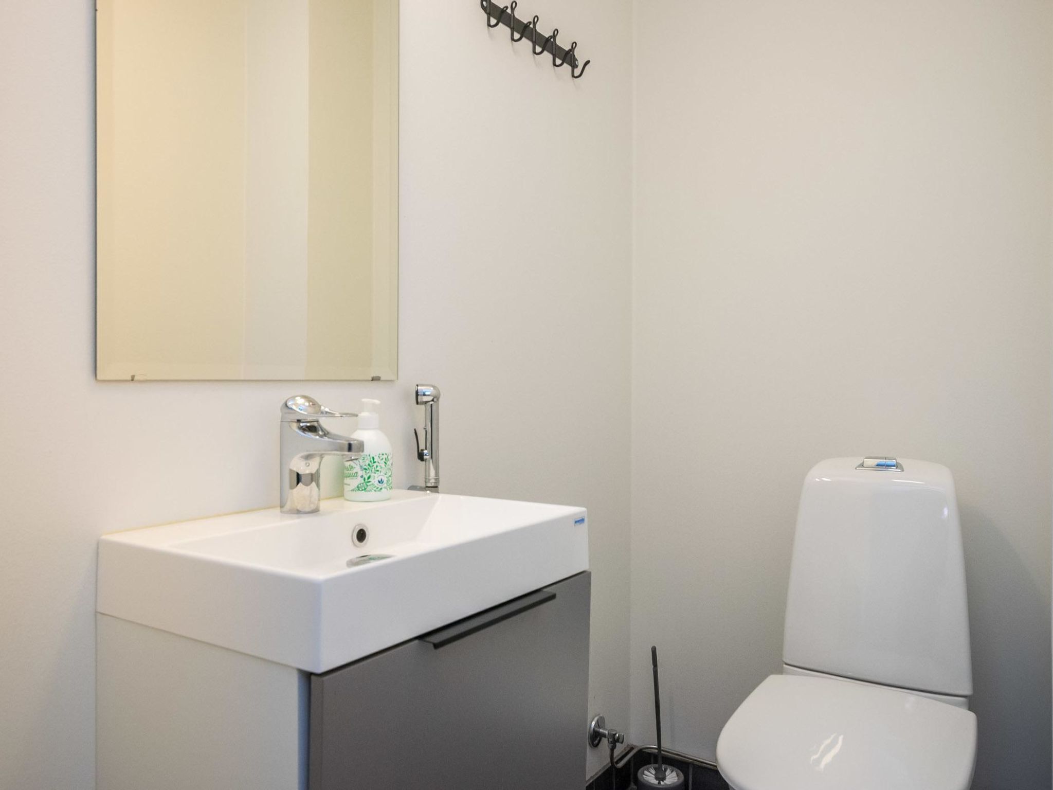 A bathroom with a white sink, a mirror, a toilet, and a soap dispenser.