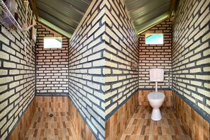 A small, enclosed bathroom with brick walls, a wooden floor, and a toilet.