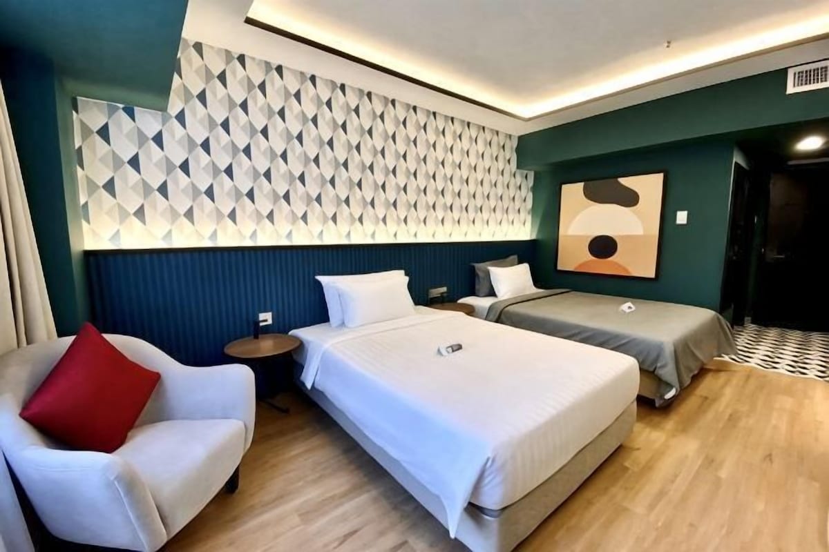 Una camera d'albergo con due letti, un divano, una parete con motivi geometrici e una porta.