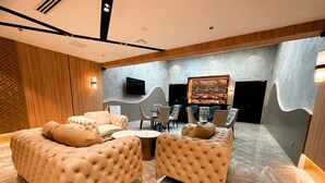 A modern lounge area with tufted sofas and armchairs, a marble floor, and a flat-screen TV mounted on the wall. - IDEAS Kuala Lumpur (Kuala Lumpur)