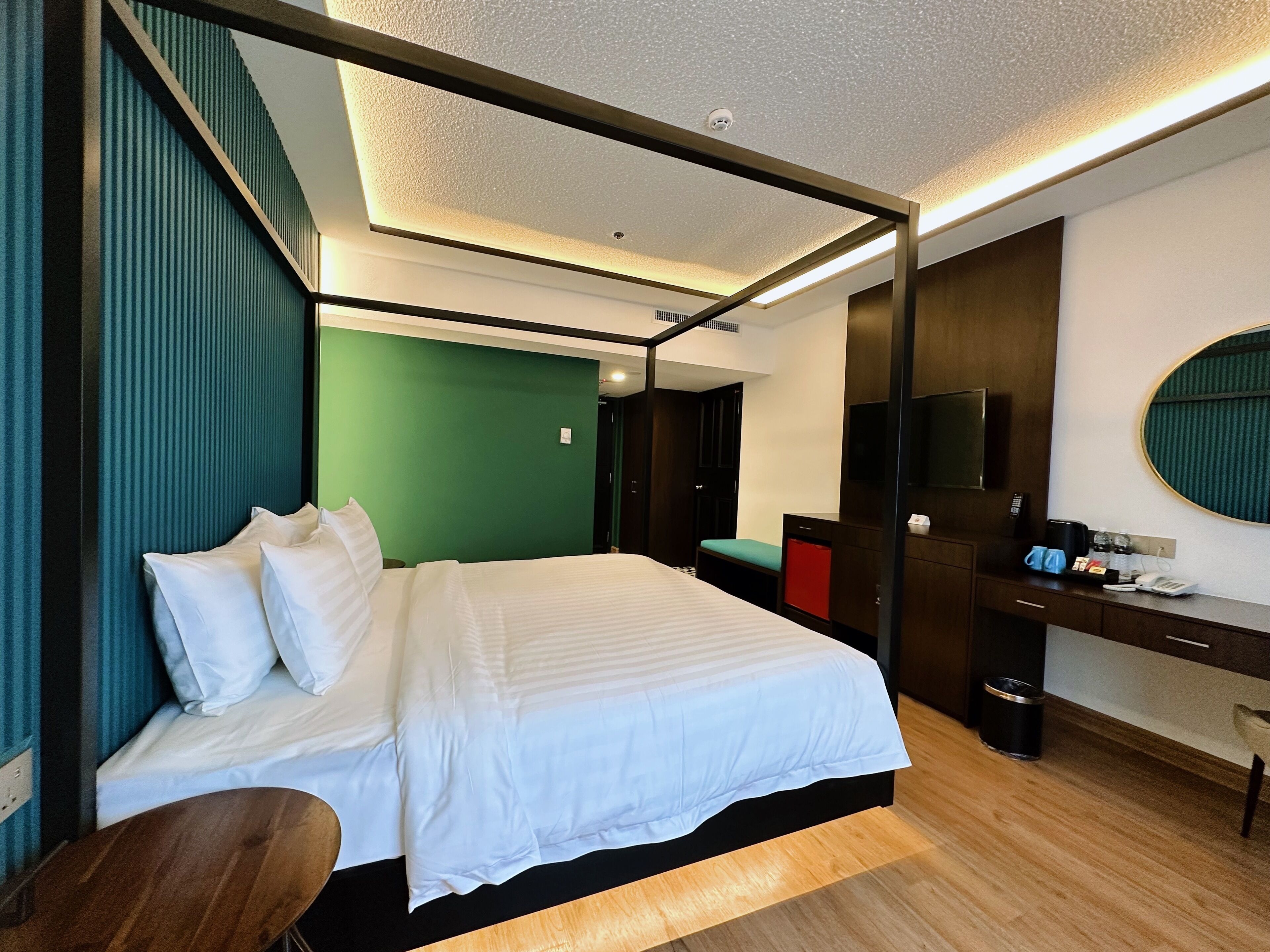 A modern hotel room with a large bed, a desk, a chair, a television, and a small seating area.
