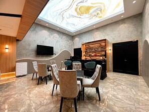 A modern dining area with marble flooring, plush chairs, a piano, and a television mounted on the wall.