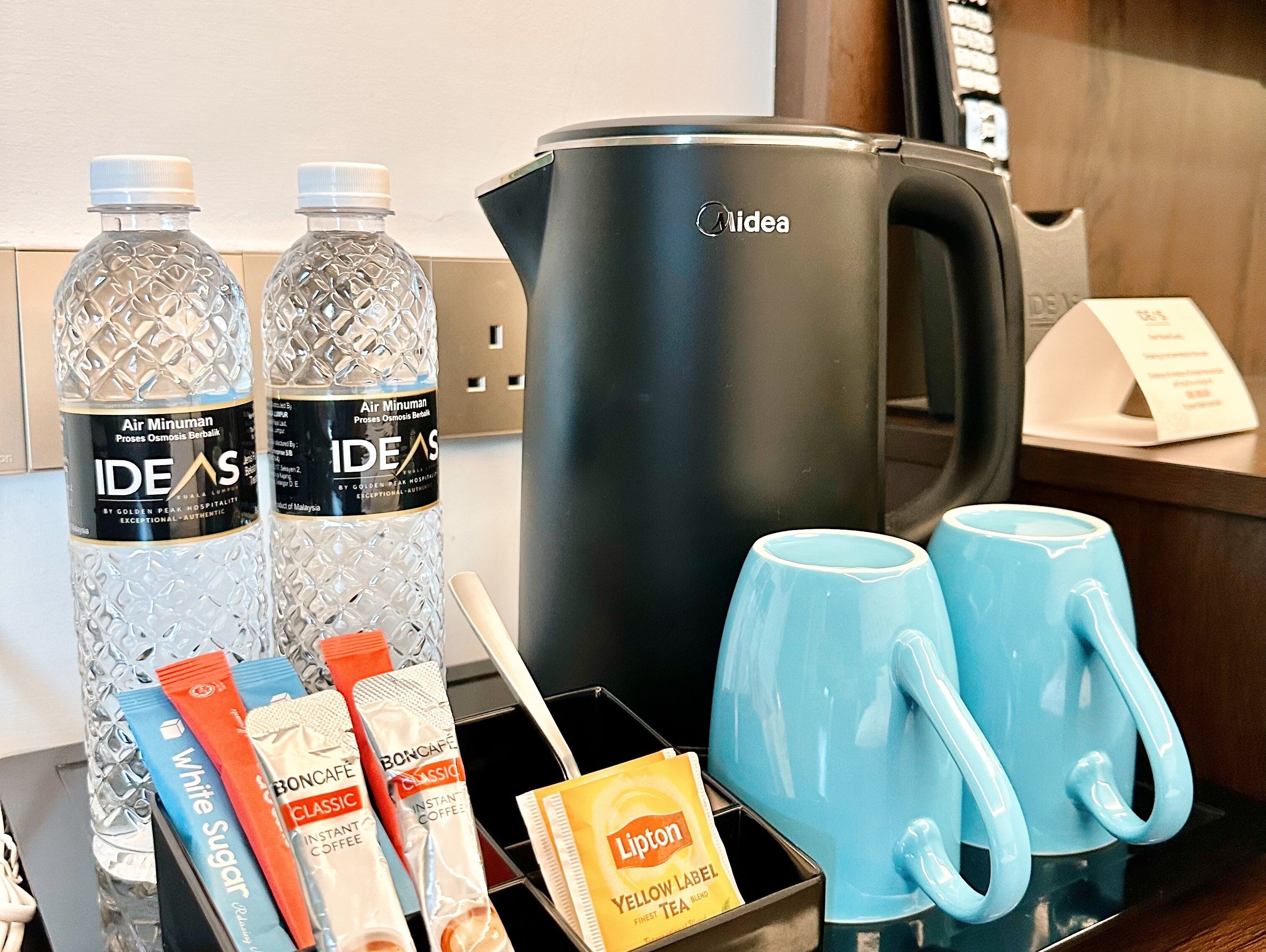 A coffee station with a Midea coffee maker, two bottles of water, a coffee dispenser, and two blue mugs.