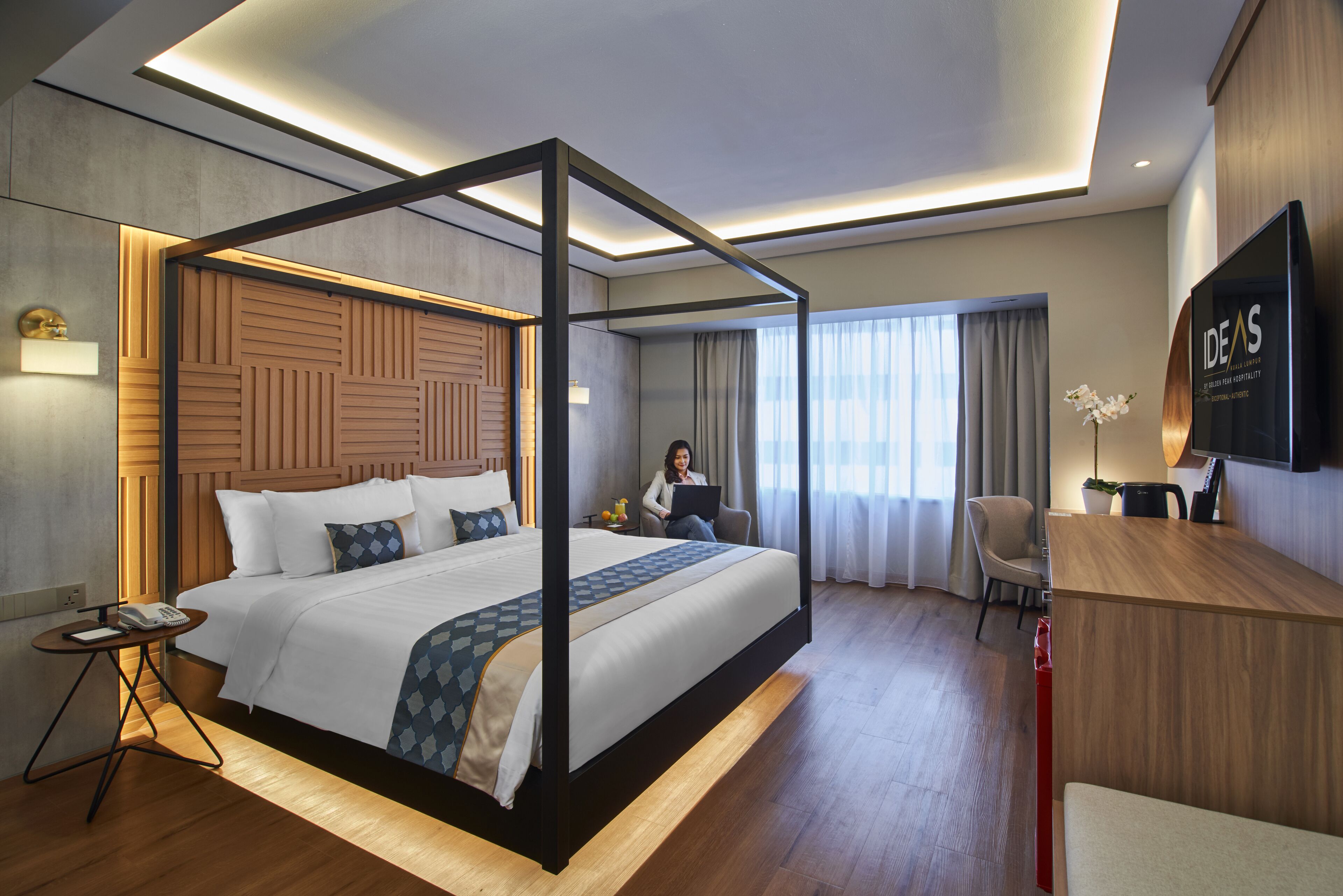 A modern hotel room with a four-poster bed, a desk, a chair, and a television.