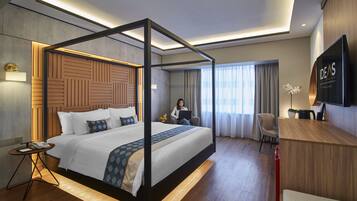 A modern hotel room with a four-poster bed, a desk, a chair, and a television.