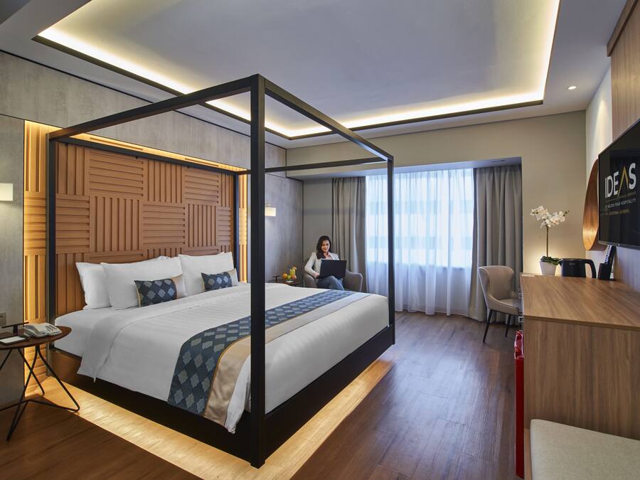 A modern hotel room with a four-poster bed, a desk, a chair, and a television.