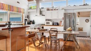 A modern kitchen with wooden beams, a bar area, and a dining space with stools. - Olde Beach Lux (Waikanae Beach)