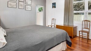 A bedroom with a bed, a desk, and chairs. There are framed pictures on the wall. - Olde Beach Lux (Waikanae Beach)