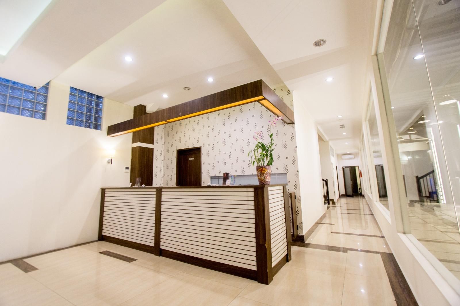 A reception area with a modern design, featuring a reception desk, a potted plant, and a patterned wall.