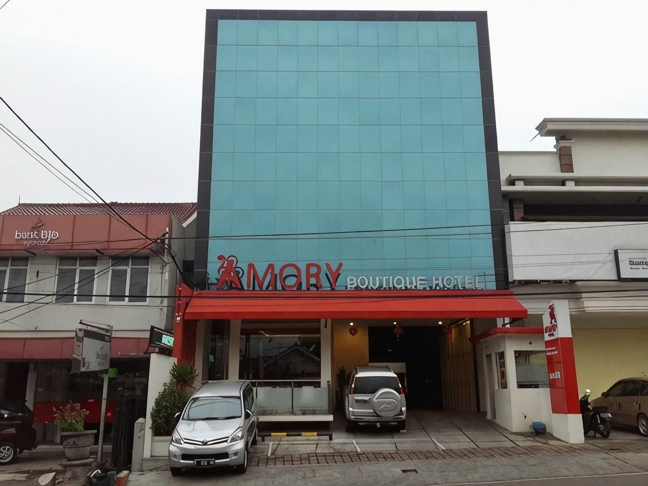 A hotel with a modern facade, a red awning, and two cars parked in front.
