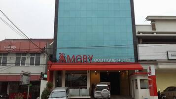 A hotel with a modern facade, a red awning, and two cars parked in front.