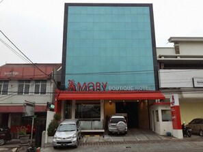 A hotel with a modern facade, a red awning, and two cars parked in front.
