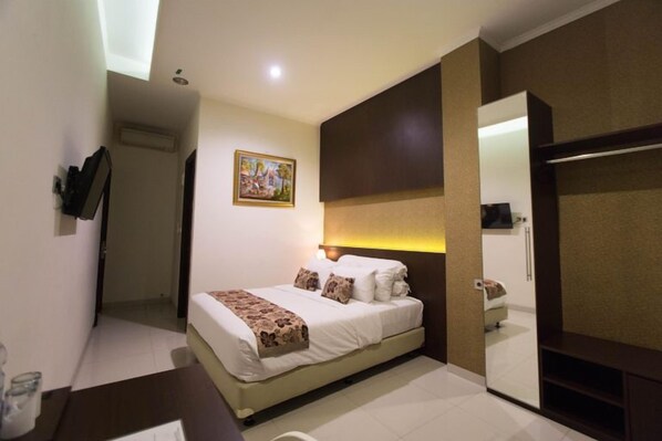 A hotel room with a bed, a bedside table, a mirror, and a door leading to another room.