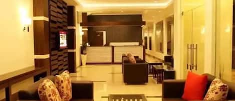 A modern hotel lobby with a reception desk, seating area, and a glass partition.