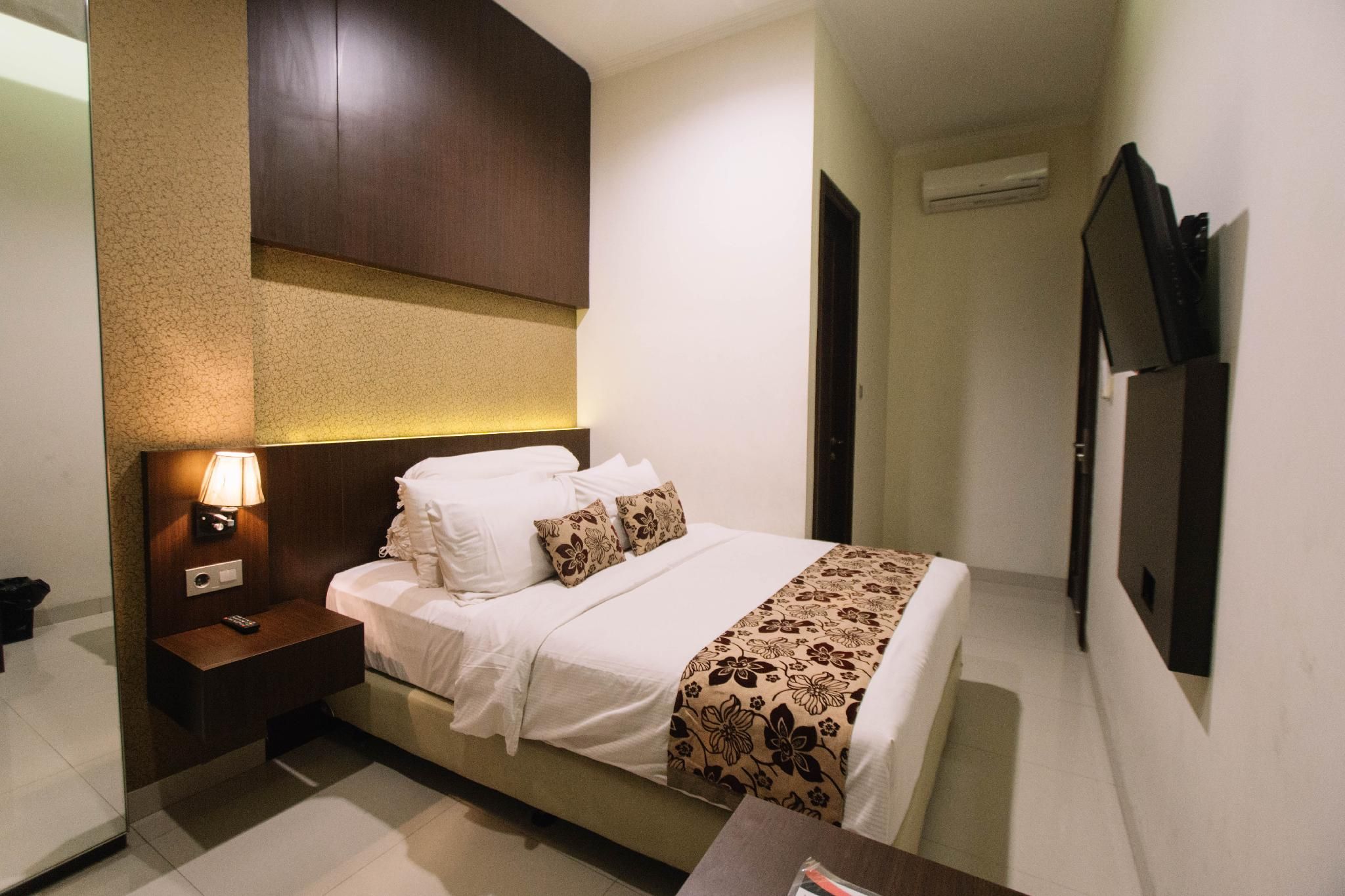 Een hotelkamer met een bed, nachtkastje, lamp en een aan de muur bevestigde televisie.