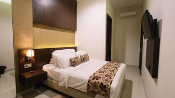 A hotel room with a bed, bedside table, lamp, and a TV mounted on the wall.