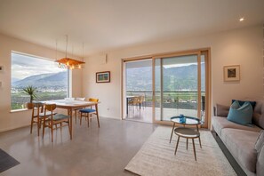 A spacious living area with a dining table, chairs, a sofa, and a balcony with a view of mountains. - Holiday Apartment "Das Eckige" with Mountain View, Wi-Fi, Garden & Terrace (Tscherms)