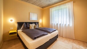Een slaapkamer met een bed, nachtkastjes, een plafondlamp, een raam met gordijnen en een aan de muur hangend schilderij.