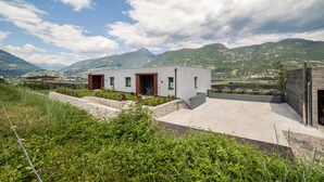 Een modern gebouw met een plat dak, een stenen keerwand en uitzicht op bergen.