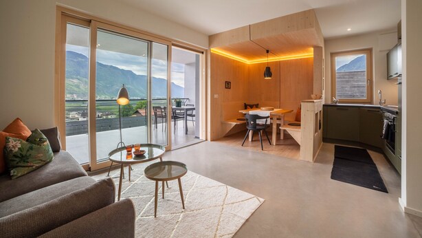 Un salon moderne avec un canapé, une table basse et une vue sur les montagnes, visible à travers de grandes portes coulissantes.