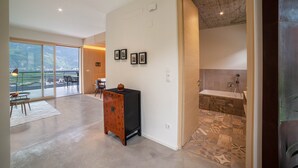 Une pièce spacieuse dotée d’une grande porte-fenêtre coulissante donnant sur un balcon, d’un petit meuble en bois et d’une salle de bain aux carreaux décoratifs.