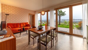 A modern living room with a sofa, dining table, chairs, and a view of the sea. - Holiday Apartment Vitus with Mountain View, Wi-Fi, Garden & Terrace (Tscherms)