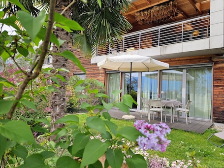 A modern house with a balcony, a dining area with outdoor furniture, and a garden with various plants and flowers.. Holiday Apartment Vitus with Mountain View, Wi-Fi, Garden & Terrace