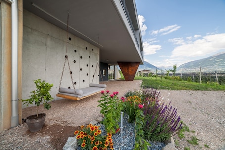 A modern building with a concrete exterior, a hanging swing, and a garden with various plants and flowers.. Holiday Apartment "Matthäus" with Mountain View, Wi-Fi, Garden & Terrace