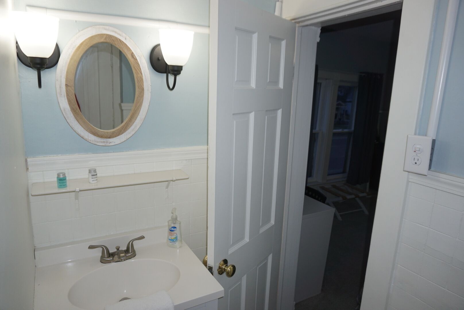 A bathroom with a white sink, a round mirror with a wooden frame, and two wall-mounted light fixtures.