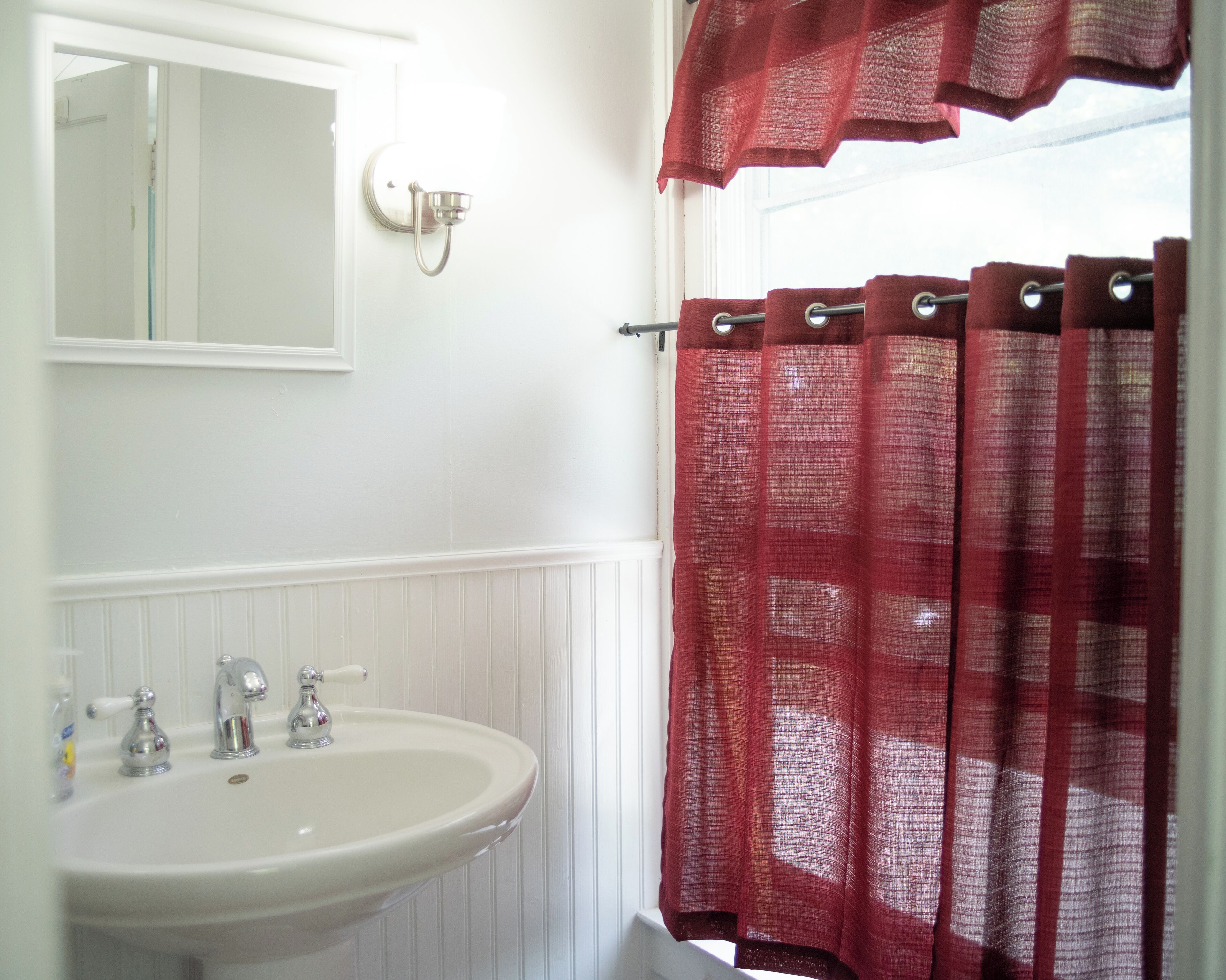 Un baño con lavamanos blanco, espejo y cortina de ducha roja.