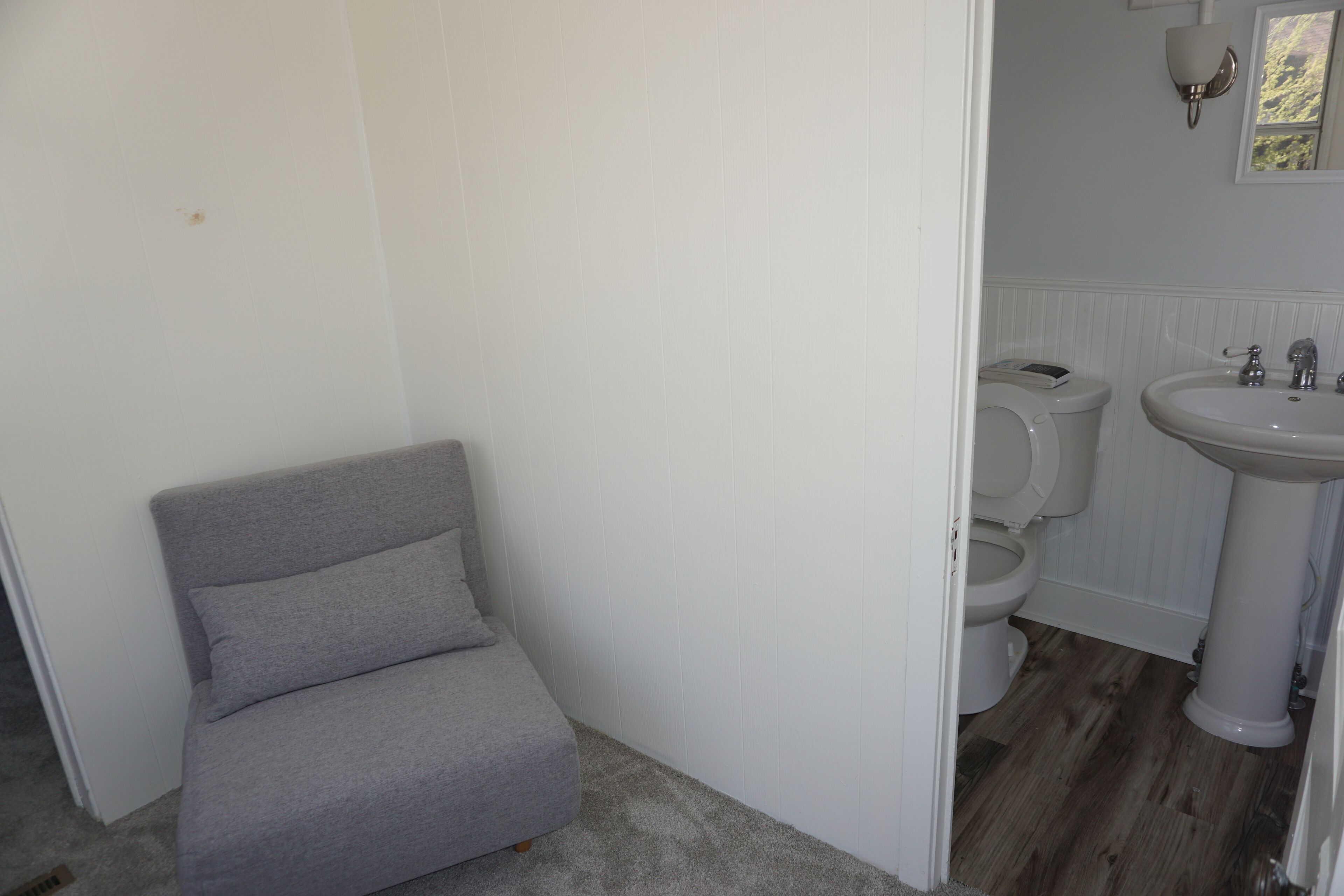 Un baño con inodoro, lavamanos y una silla gris.