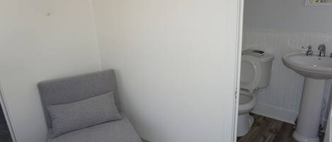 A bathroom with a toilet, sink, and a grey chair.